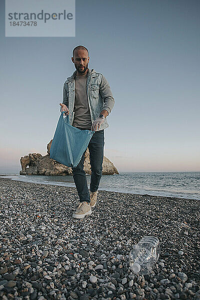 Mann mit Plastiktüte sammelt Müll vom Strand