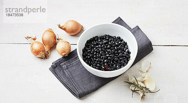 Studio shot of bowl of black beans  raw onions  garlic and rosemary