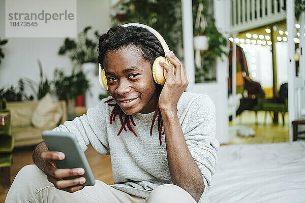 Glücklicher Mann benutzt Smartphone und hört zu Hause Musik über Kopfhörer