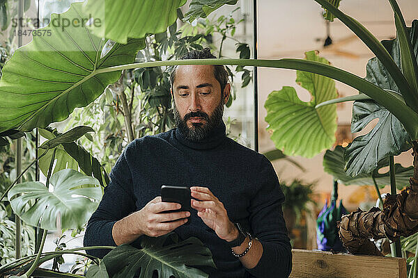 Reifer Mann benutzt Smartphone inmitten von Pflanzen