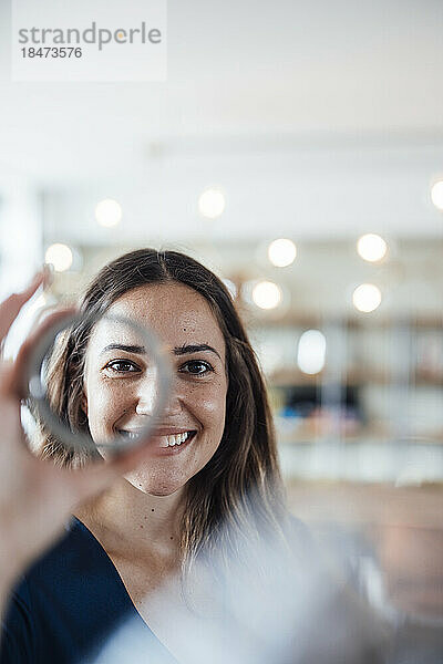 Lächelnde Geschäftsfrau  die im Büro durch kreisförmige Geräte schaut