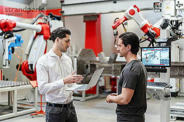 Kollege erklärt Techniker über Laptop in Roboterfabrik