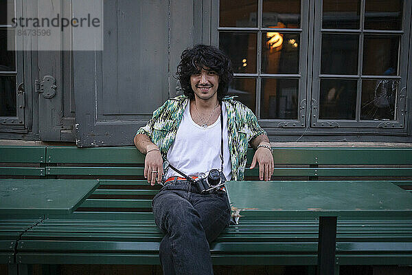 Glücklicher junger Mann  der auf einer Bank sitzt