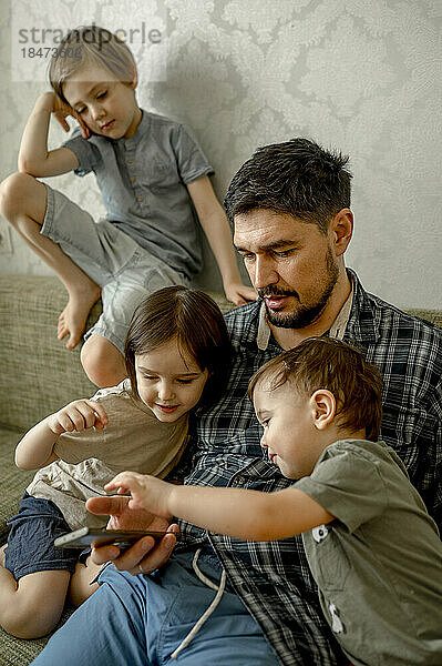 Vater und teilendes Smartphone mit Kindern auf dem Sofa zu Hause