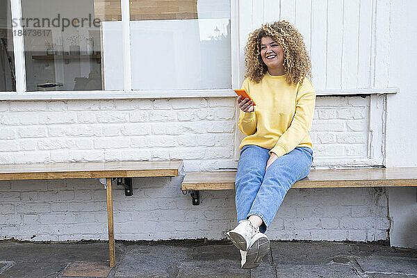 Glückliche Frau mit Smartphone sitzt auf Bank