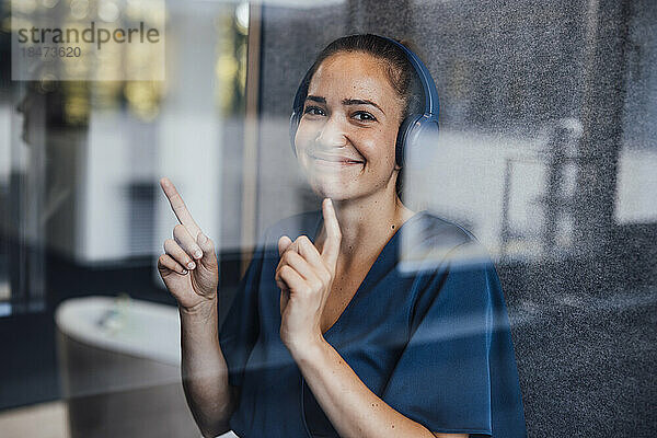 Lächelnde junge Geschäftsfrau gestikuliert durch Glas gesehen