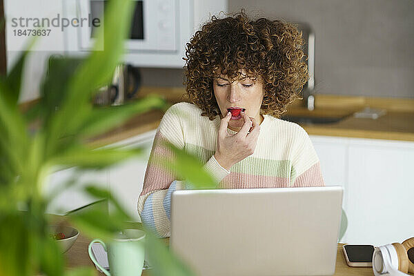 Freiberufler isst Himbeeren und arbeitet zu Hause am Laptop