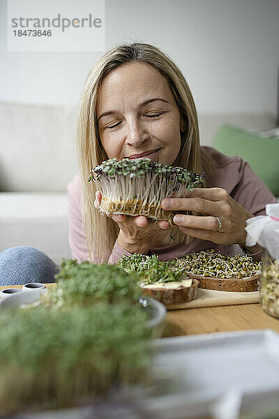 Lächelnde Frau mit geschlossenen Augen  die zu Hause selbst angebaute Kräuter riecht