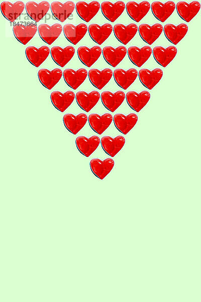 Rows of heart shaped candy flat laid against green background