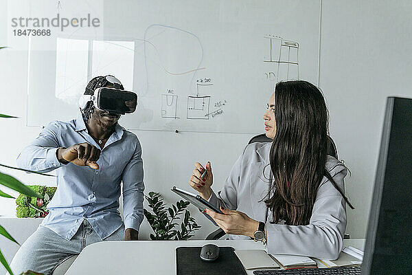 Architekt hält Tablet-PC in der Hand und diskutiert mit Kollegen  der im Büro ein Virtual-Reality-Headset trägt
