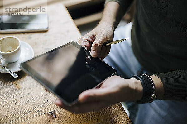 Hände eines Mannes mit Tablet-PC auf dem Tisch im Café