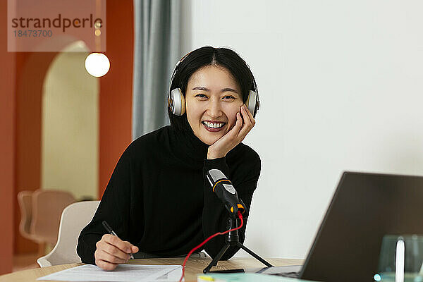 Glückliche Frau mit Kopfhörern sitzt im Podcast-Studio