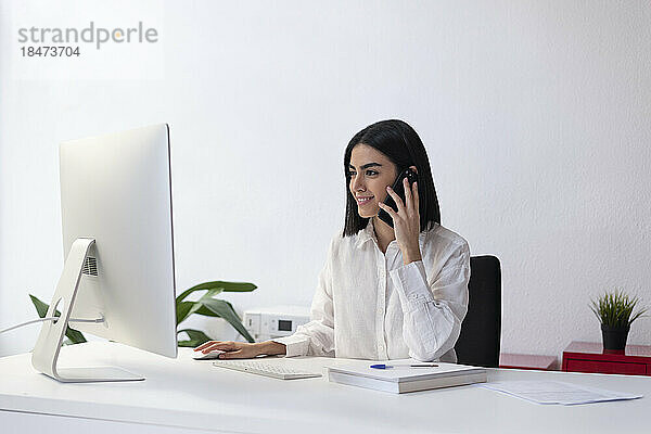 Lächelnde junge Geschäftsfrau  die am Schreibtisch mit dem Smartphone spricht