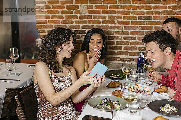 Glückliche Frau teilt Smartphone mit Freunden im Restaurant