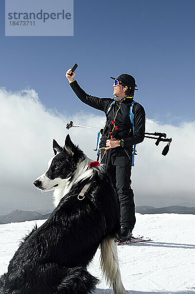 Mann macht Selfie mit Smartphone und Hund sitzt im Schnee