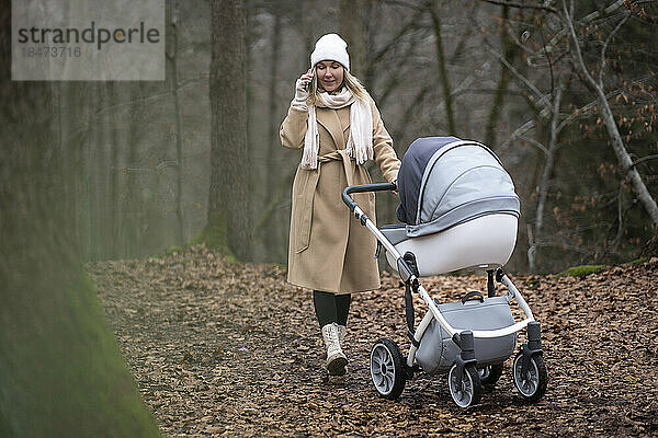 Frau mit Kinderwagen telefoniert im Wald