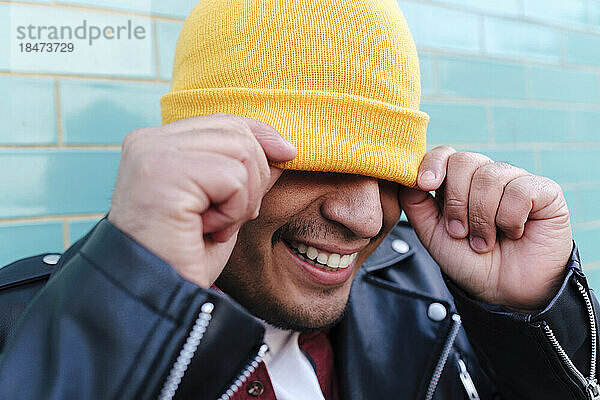 Lächelnder Mann bedeckt Gesicht mit gelber Strickmütze