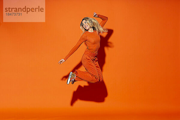Glückliche Frau springt vor orangefarbenem Hintergrund