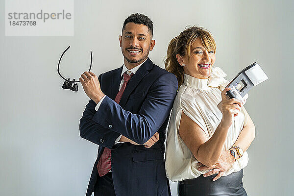 Happy business partners standing with equipment against white background