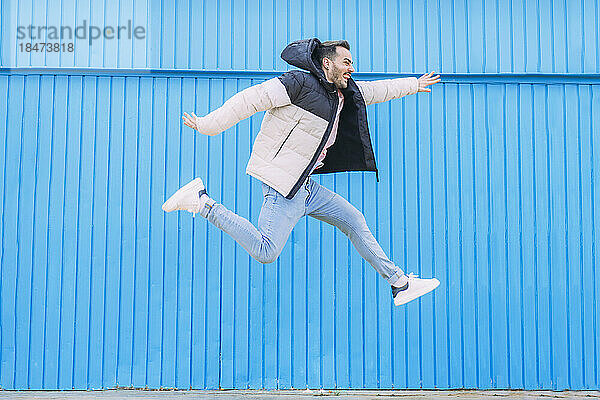 Fröhlicher Mann springt vor blaue Wand