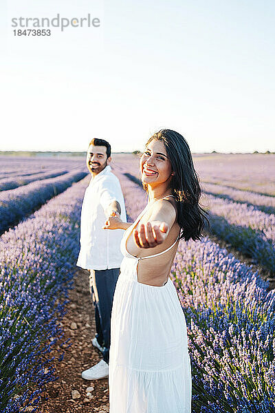 Happy young woman gesturing standing in field holding hands with boyfriend