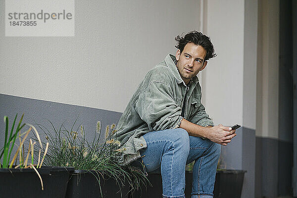 Young man sitting by potted plants with smart phone