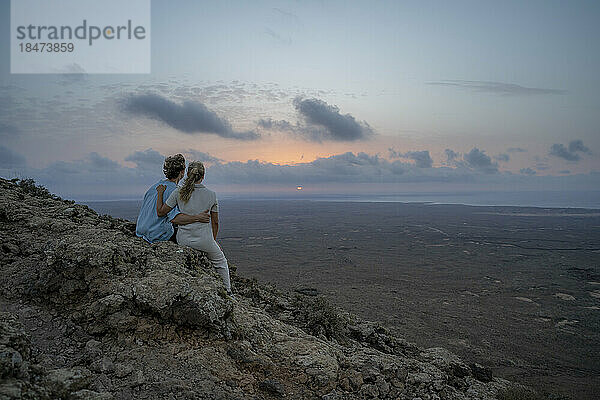 Ein Paar blickt auf den Sonnenuntergang und sitzt auf einem Berg