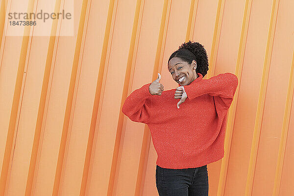 Glückliche Frau gestikuliert vor orangefarbener Wand