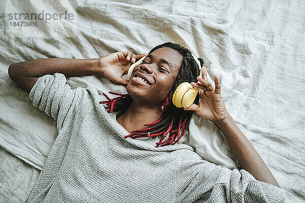 Glücklicher Mann mit Kopfhörern  der zu Hause im Bett Musik hört