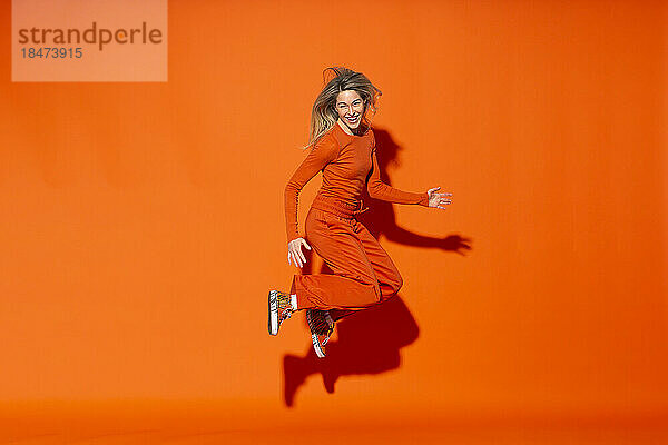 Fröhliche Frau springt vor orangefarbenem Hintergrund