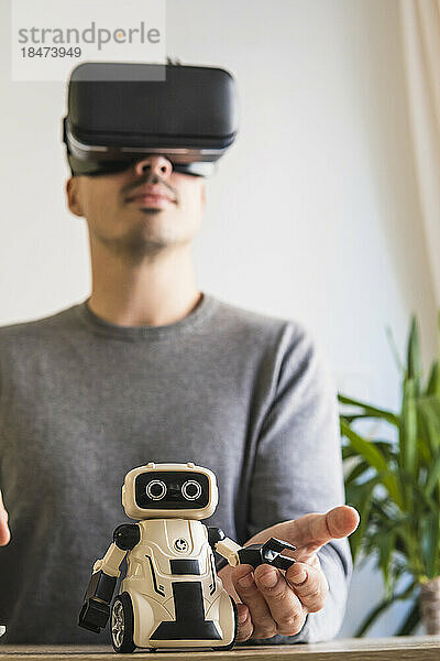 Geschäftsmann mit VR-Brille analysiert Spielzeugroboter im Büro