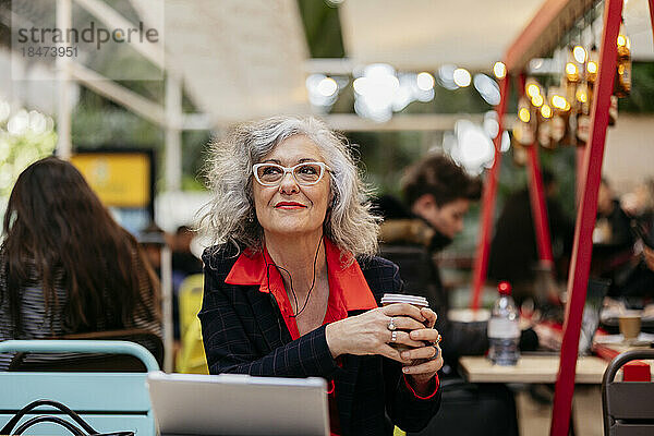Nachdenkliche Geschäftsfrau sitzt mit Einwegkaffeetasse im Café
