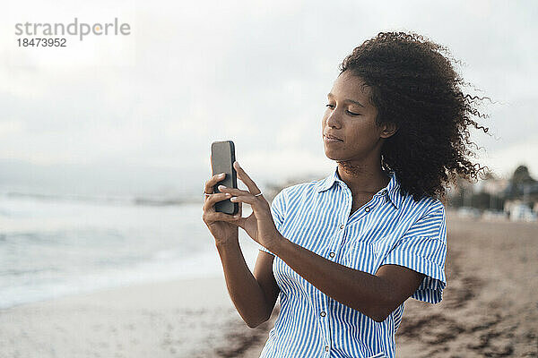 Junge Frau fotografiert mit Smartphone am Strand