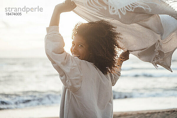 Fröhliche junge Frau mit Schal am Strand