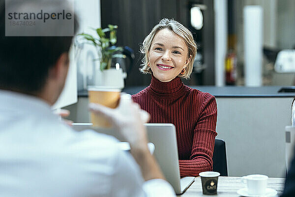 Lächelnde Geschäftsfrau diskutiert mit Kollegen am Schreibtisch