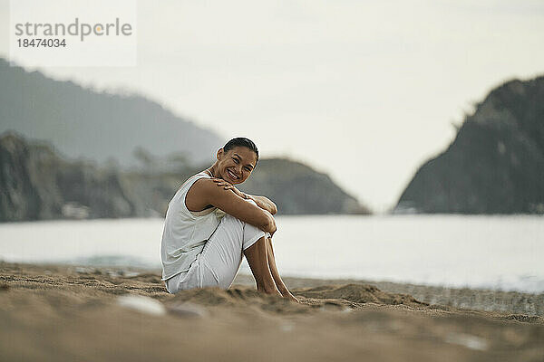 Glückliche Frau sitzt auf Sand am Strand