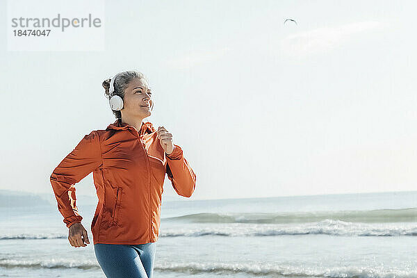 Lächelnde reife Frau joggt am Strand