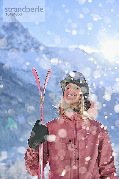 Glückliche Frau mit Skiern  die an einem sonnigen Tag vor dem Berg steht