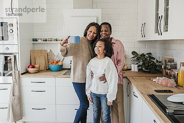 Frau macht Selfie mit Mutter und Tochter per Smartphone in der heimischen Küche