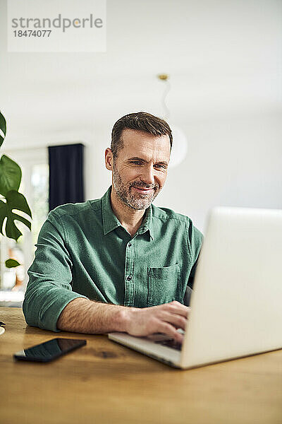 Geschäftliches Arbeiten mit Laptop von zu Hause aus am Tisch sitzend