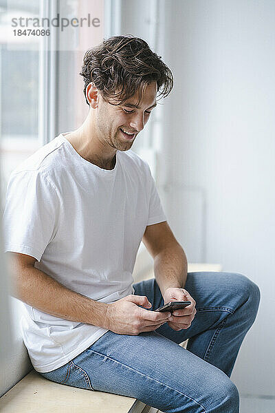 Happy young man using smart phone by window