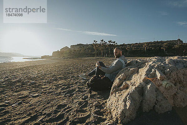 Nachdenklicher Mann sitzt an einem Felsen am Strand