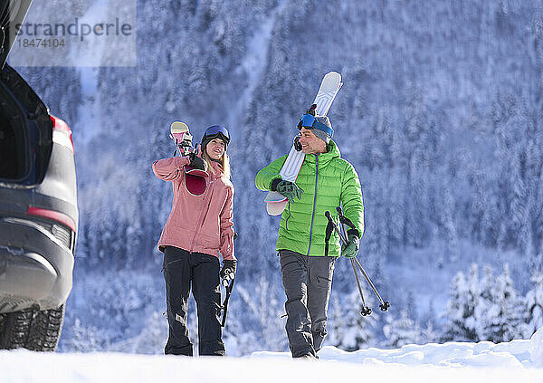 Mann und Frau laufen mit Skiern und Stöcken vor dem Berg