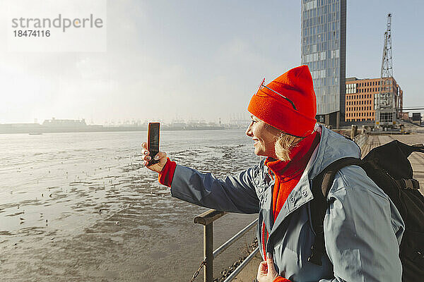 Frau fotografiert Fluss mit Smartphone