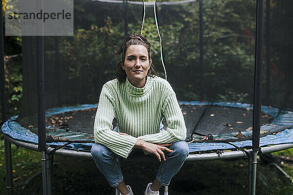 Lächelnde Frau sitzt auf dem Trampolin