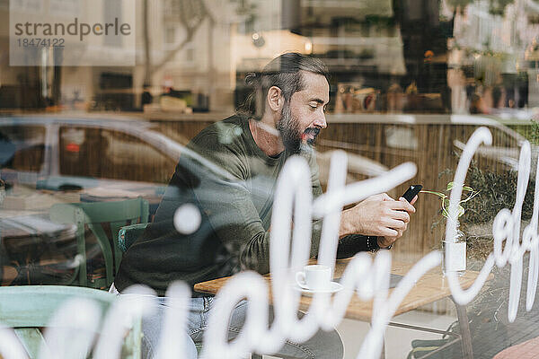 Mann benutzt Smartphone im Café  gesehen durch Glas