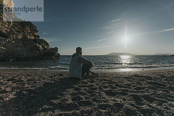 Nachdenklicher Mann sitzt bei Sonnenuntergang am Strand