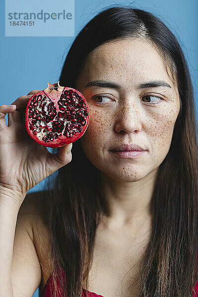 Frau hält Granatapfel vor blauem Hintergrund