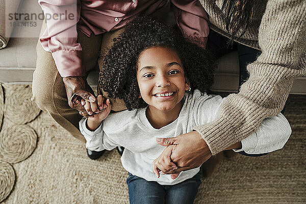Smiling girl holding hands with mother and grandmother at home