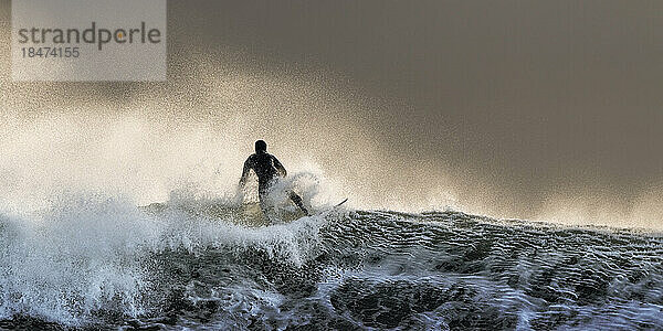 Sorgloser Surfer surft bei Sonnenuntergang auf dem welligen Meer